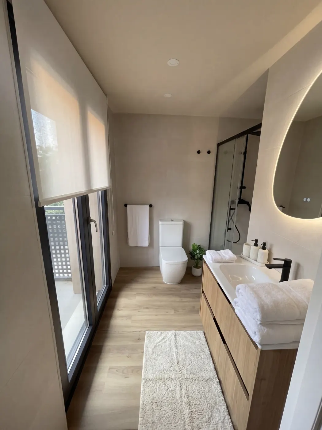 Hotel bathroom with shower, backlit mirror and wooden vanity