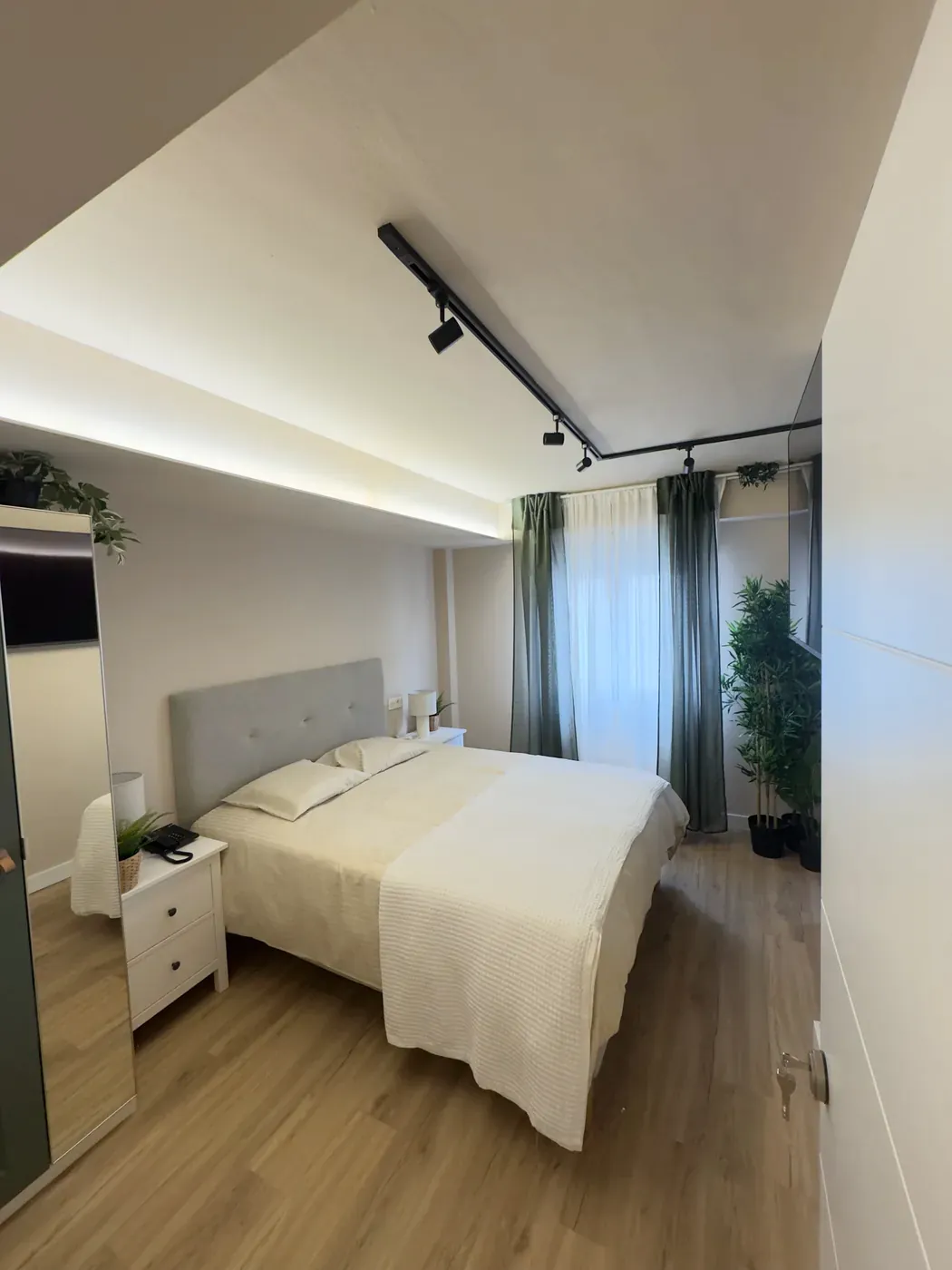 Bed in the double room, with green curtains by the window