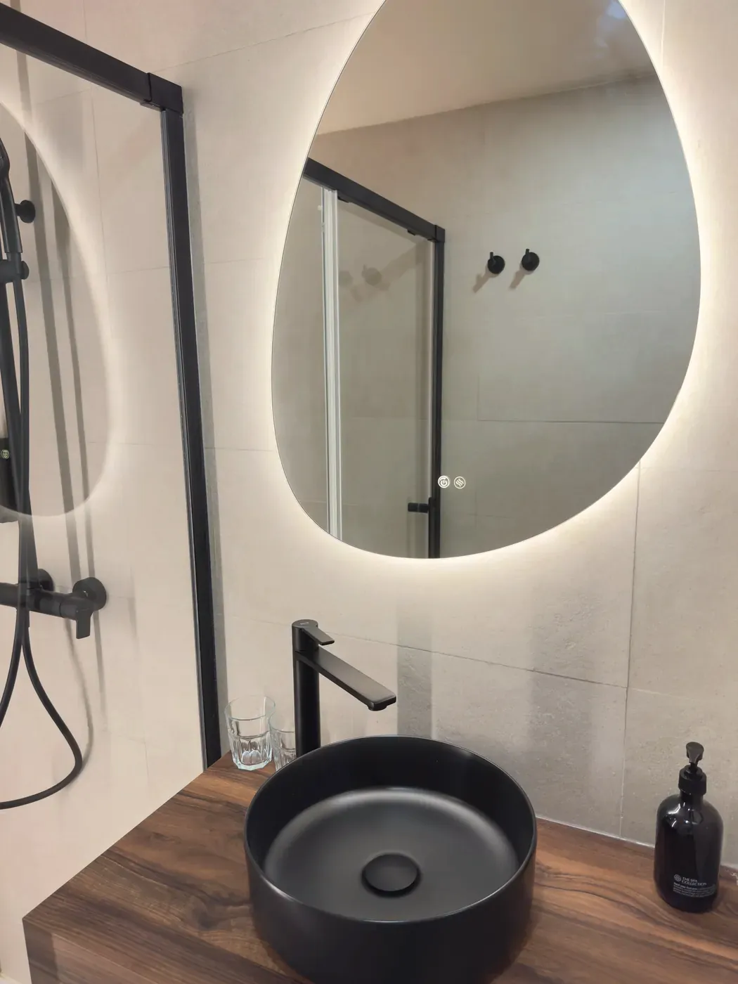 Black washbasin on a wooden counter with an illuminated mirror