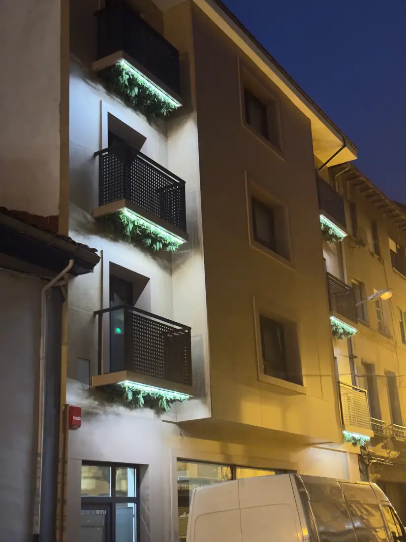Fachada del hotel de noche, con las luces verdes de los balcones encendidas