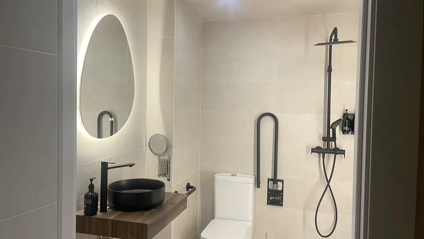 Bathroom with washbasin on a wooden shelf, toilet with fold-down grab bar and flush-floor shower
