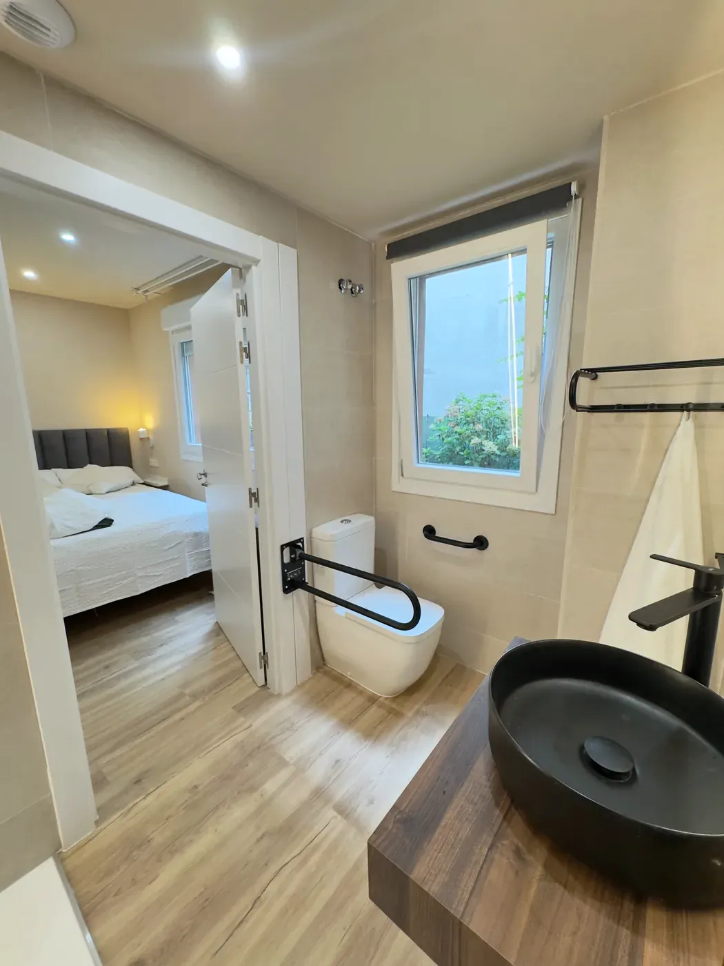 Bathroom with grab bars beside the toilet, seen from the bedroom